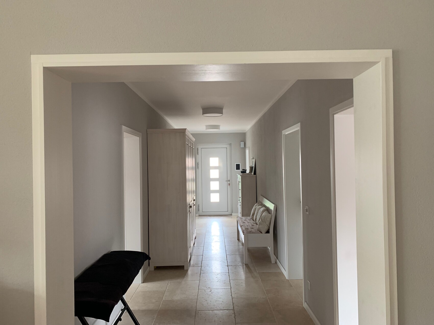 Bright hallway with gray walls, wardrobe on the left, bench with cushions on the right, door at the end.