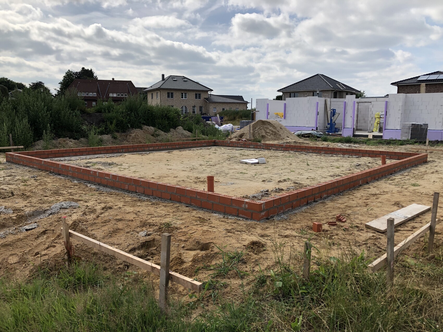 Foundation made of bricks in a rectangular trench, sandy soil, construction equipment in the background