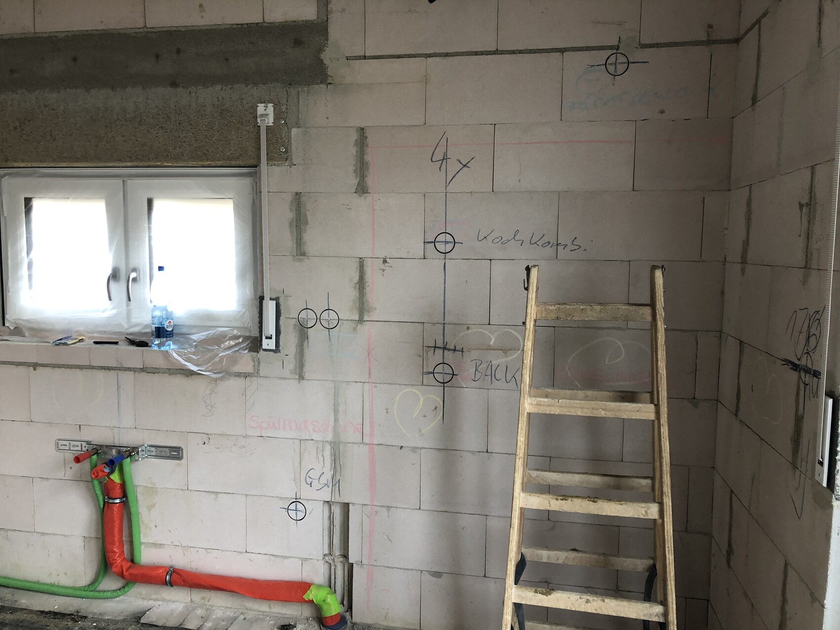 Unfinished block wall, wooden ladder, red/green pipes, markings and window.