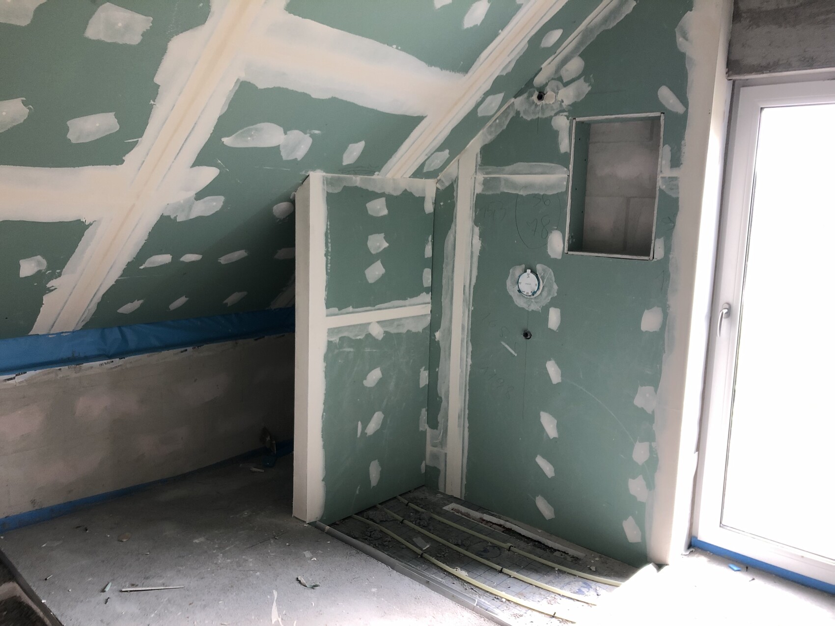 Unfinished attic construction with green drywall panels, sloped ceiling, glass door and ongoing work.