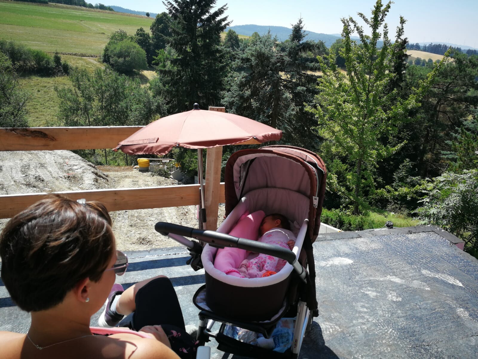 Woman with stroller, sleeping baby in a pink sleeping bag under a pink sunshade on the terrace.