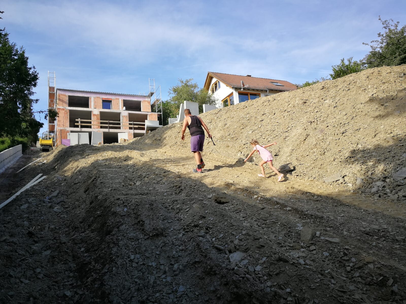 Two people climbing an earth mound at a construction site; a shell structure in the background.