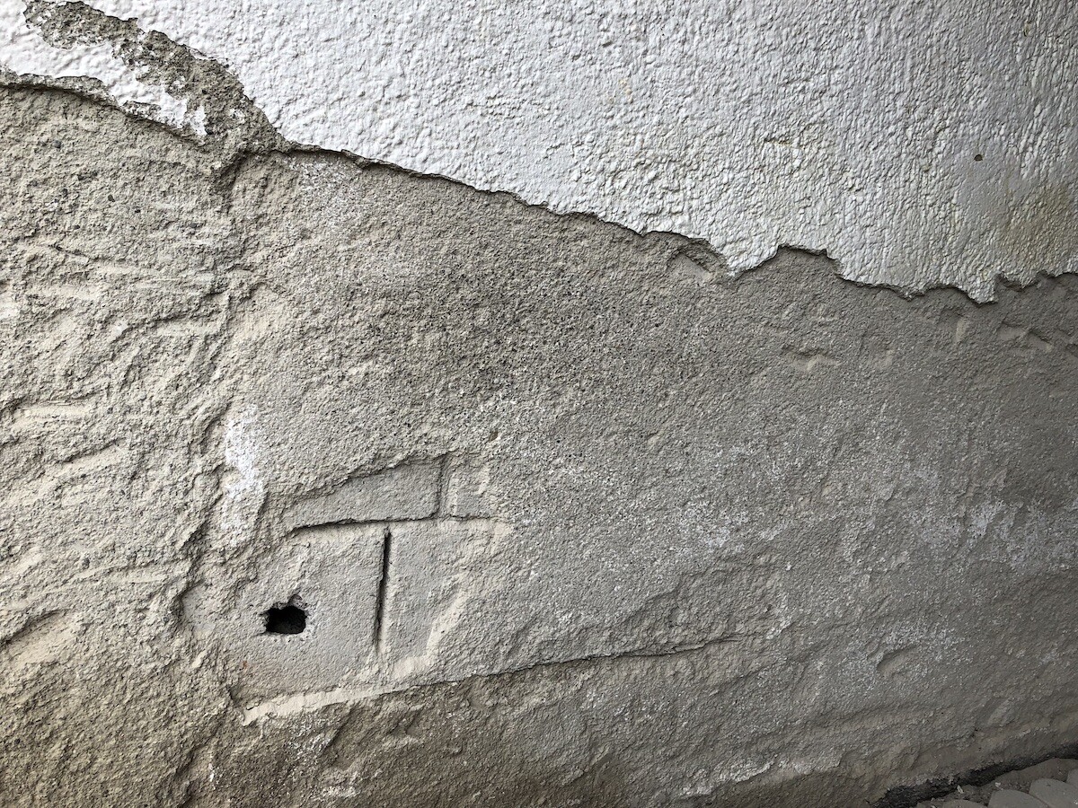 Grey plastered wall with peeling plaster, small hole, and rectangular recess.