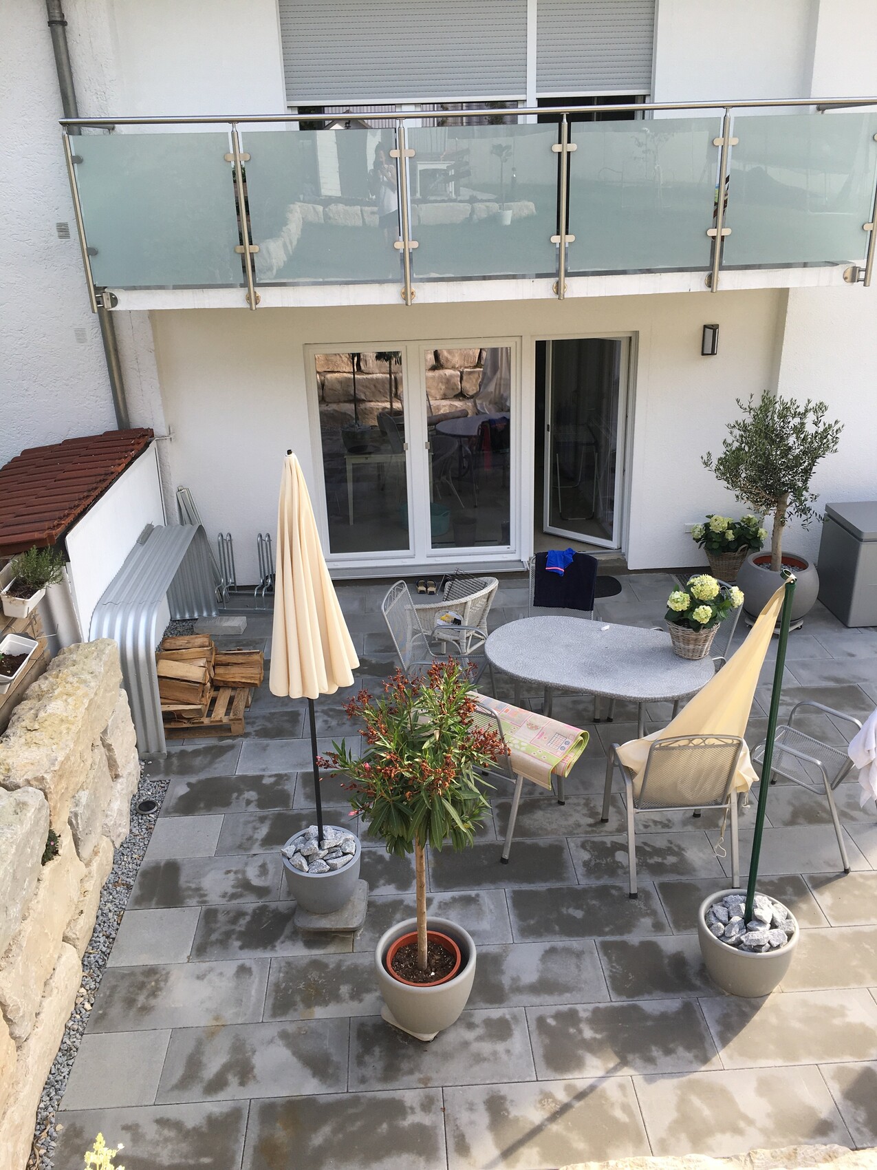 Terrace with glass railing, dining table, chairs, parasols and potted plants