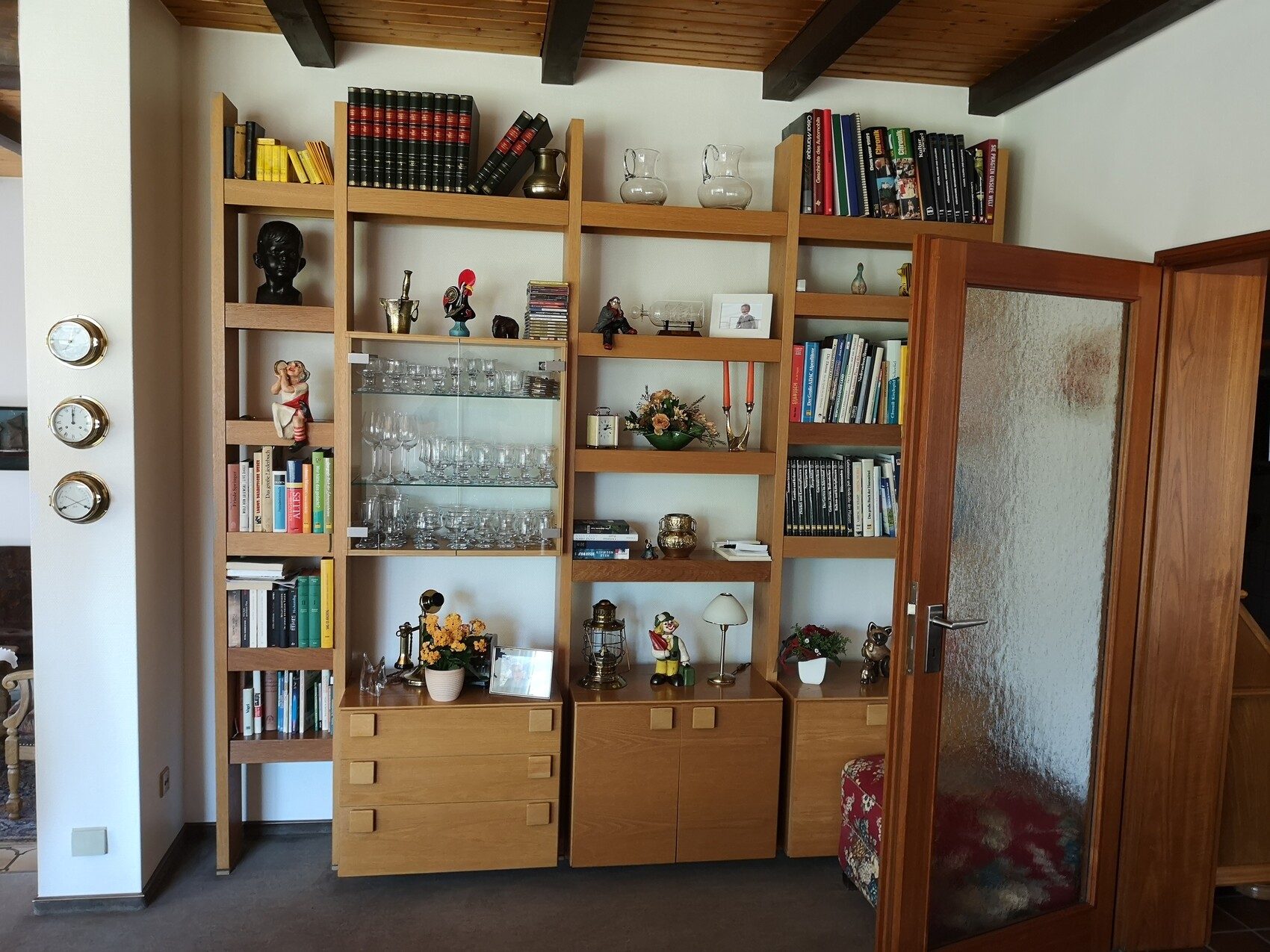 Holzregale in Wohnzimmer mit Büchern, Gläsern und Deko-Figuren; Tür mit milchigem Glas rechts.