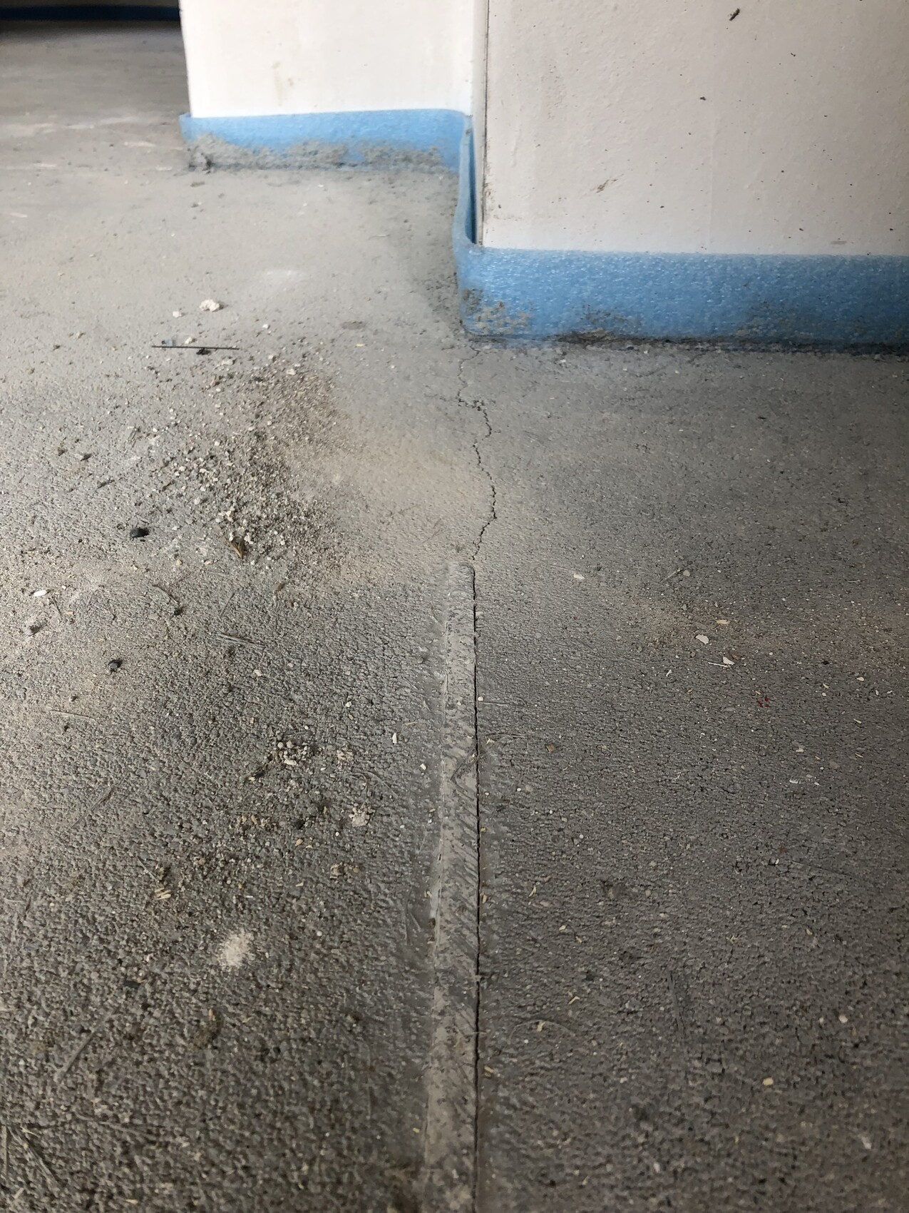 Boden mit Riss und Staub, weiße Wand mit blauer Sockelleiste in einer Ecke.