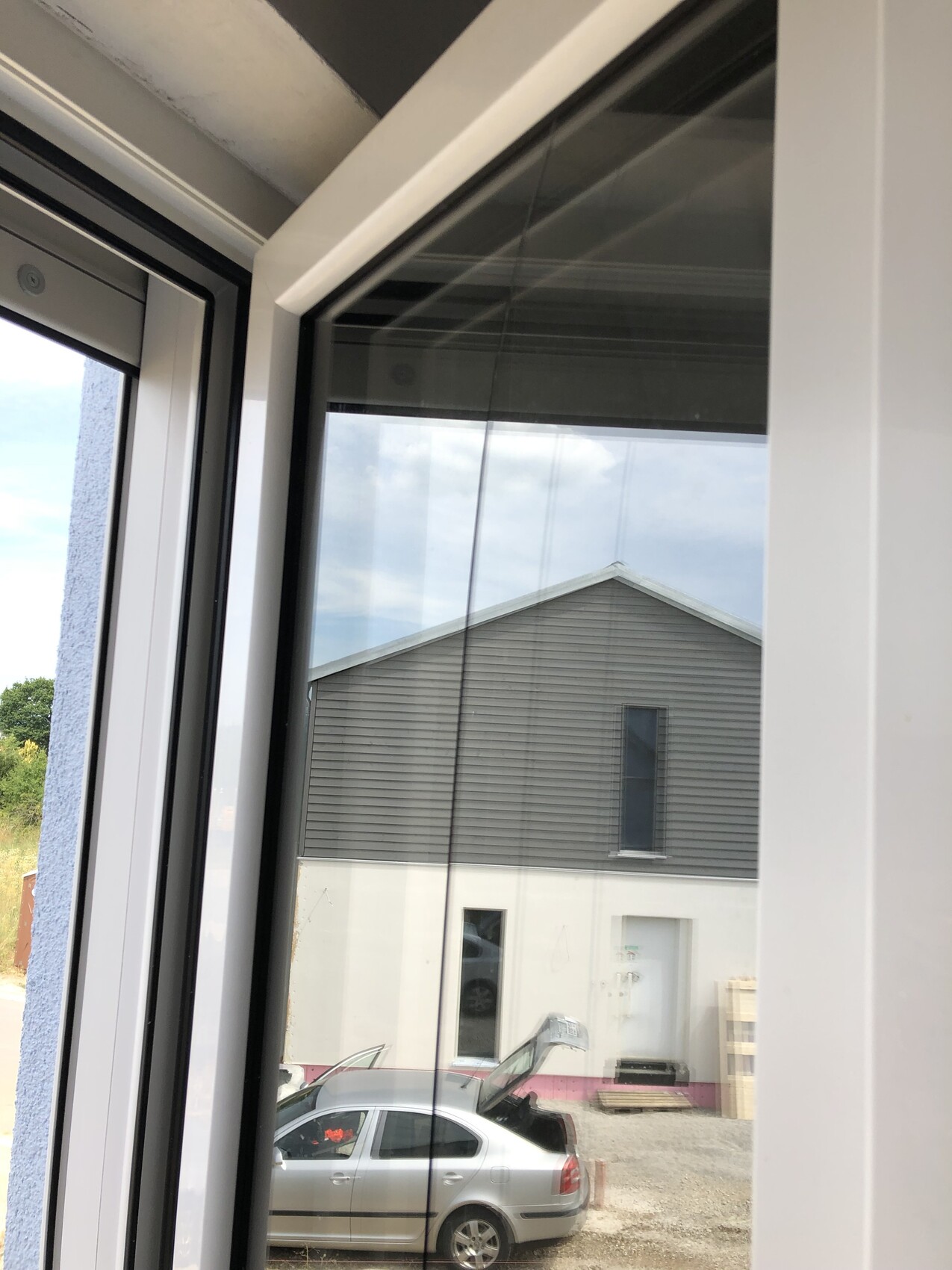 View through window onto gray building with dark facade, door below, silver car in front