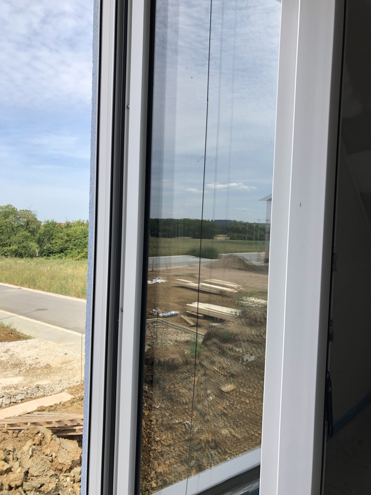 View from window onto construction site: soil, stack of boards, construction wood; background forest and sky.
