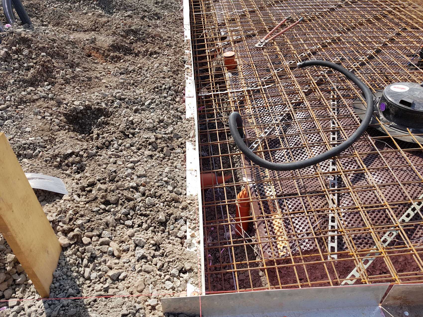 Bewehrungsstahl-Gitter über Fundamentrahmen auf Baustelle, Erdaushub und Kies daneben.