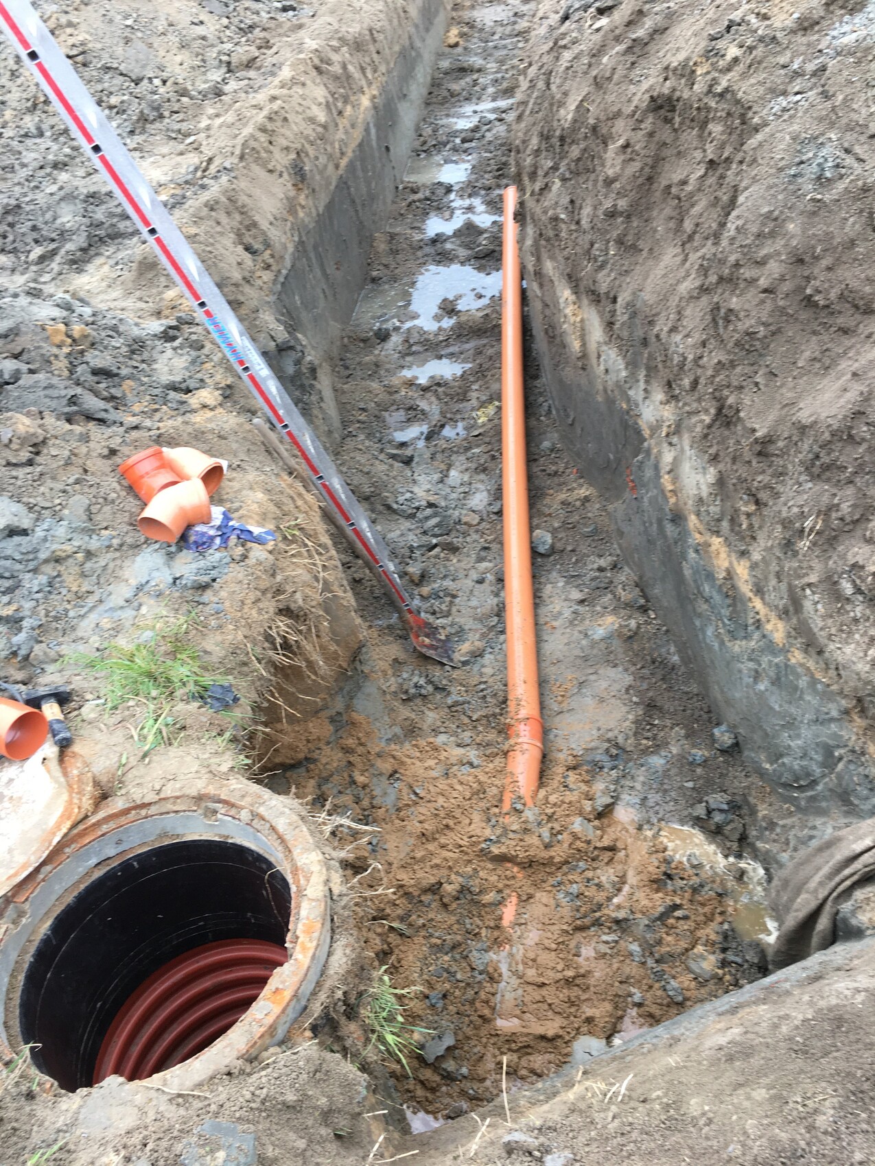 Open excavation pit with orange piping and red spiral pipe in the shaft, muddy ground.