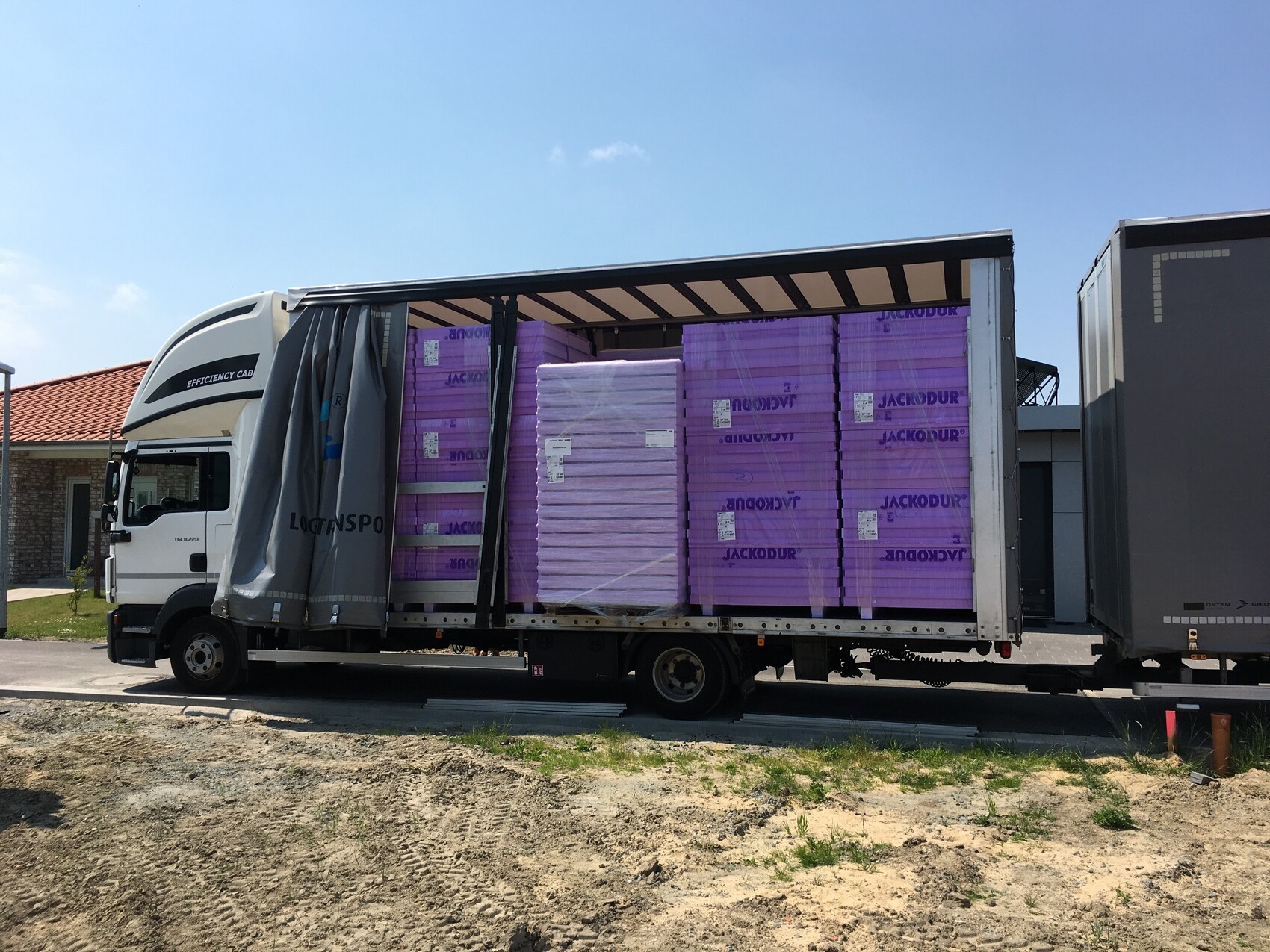 Truck with open side loaded with stacked purple JACKODUR insulation boards in the trailer.