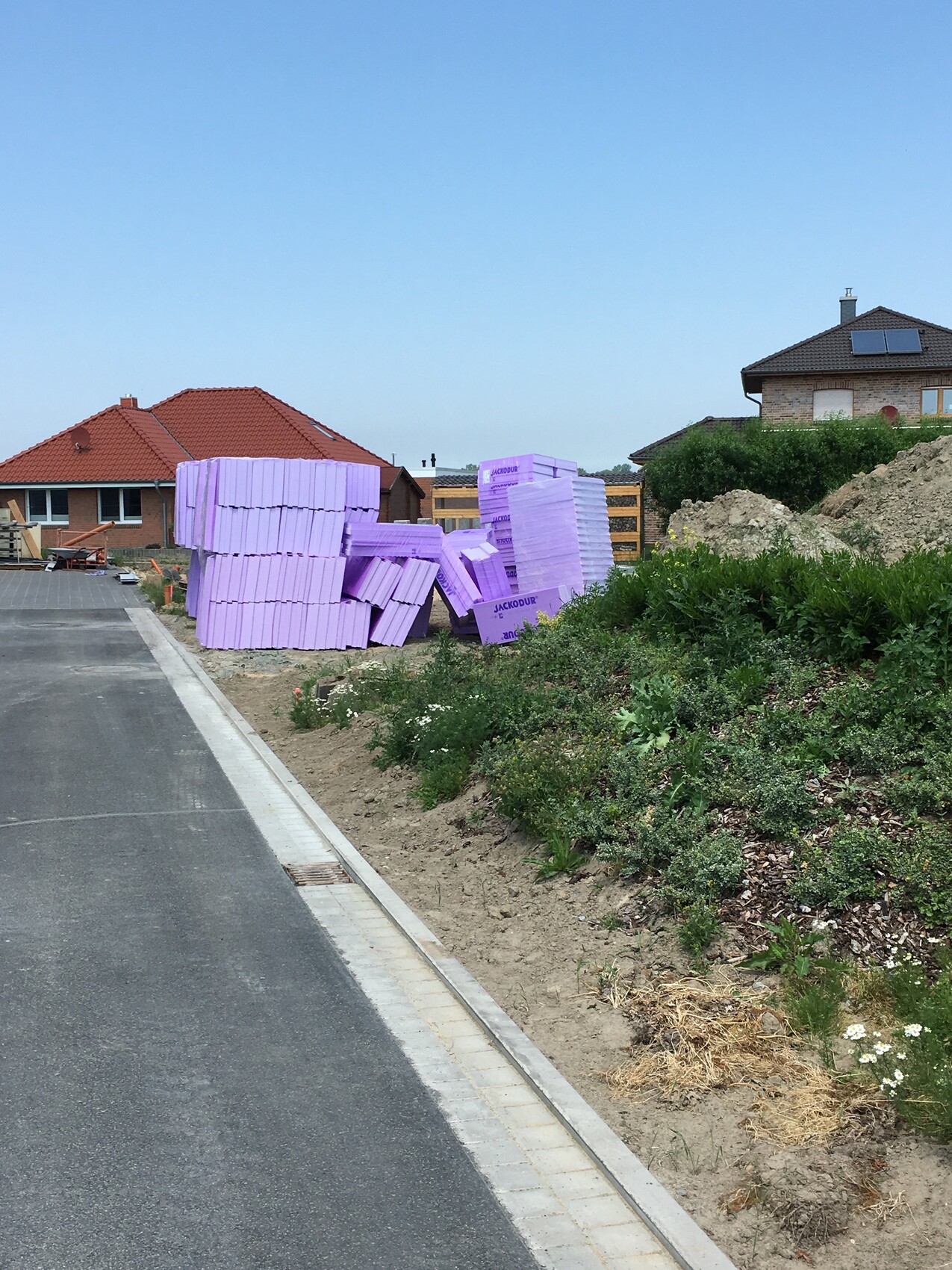 Stack of purple polystyrene insulation boards on pallets next to a street on a construction site.
