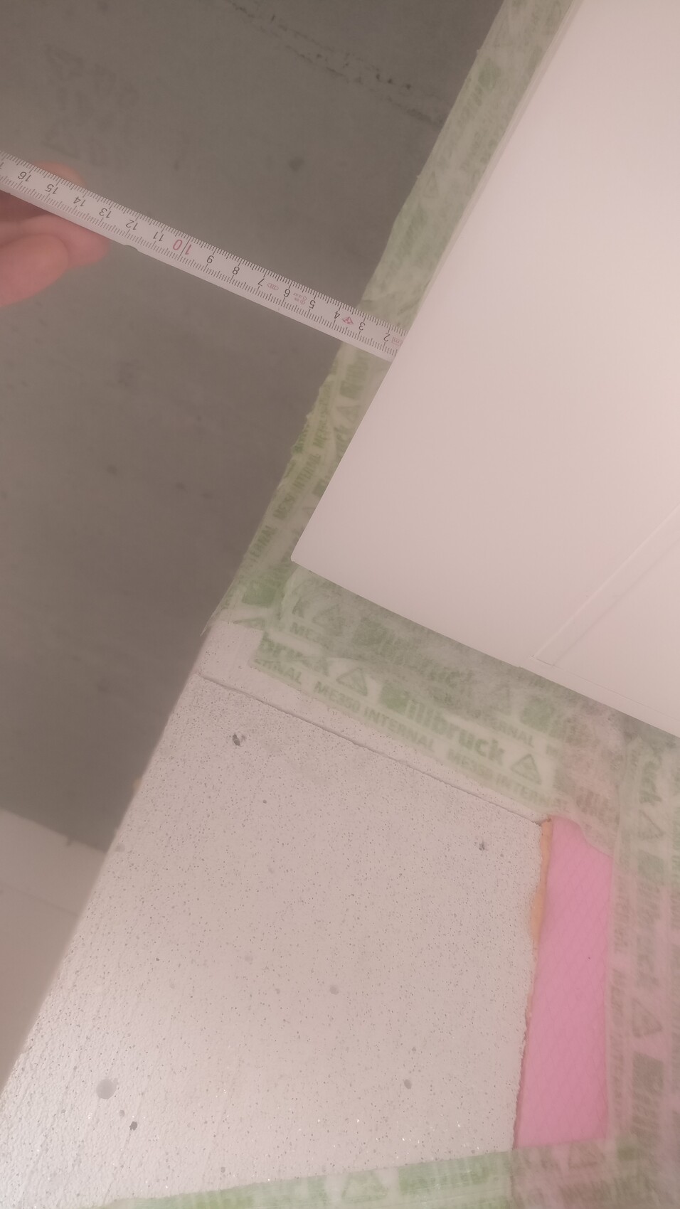 Close-up of a tape measure in interior finishing, green-white sealing tape and pink insulation panel visible