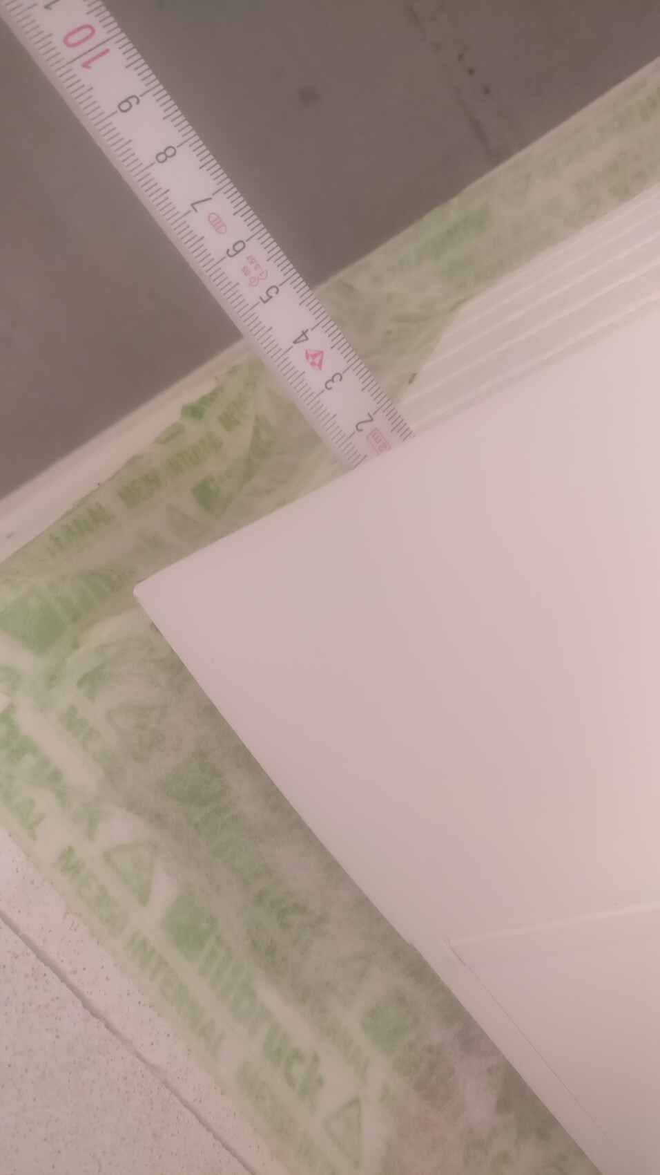 Close-up of a tape measure on floor tiles next to a white panel on a construction site