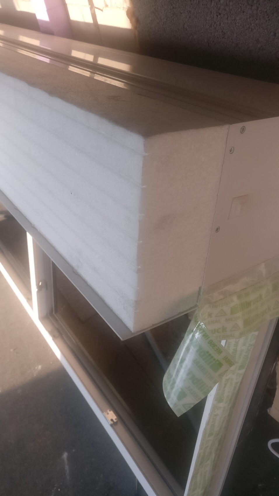 Close-up of a window frame with white polystyrene insulation block and adhesive tape