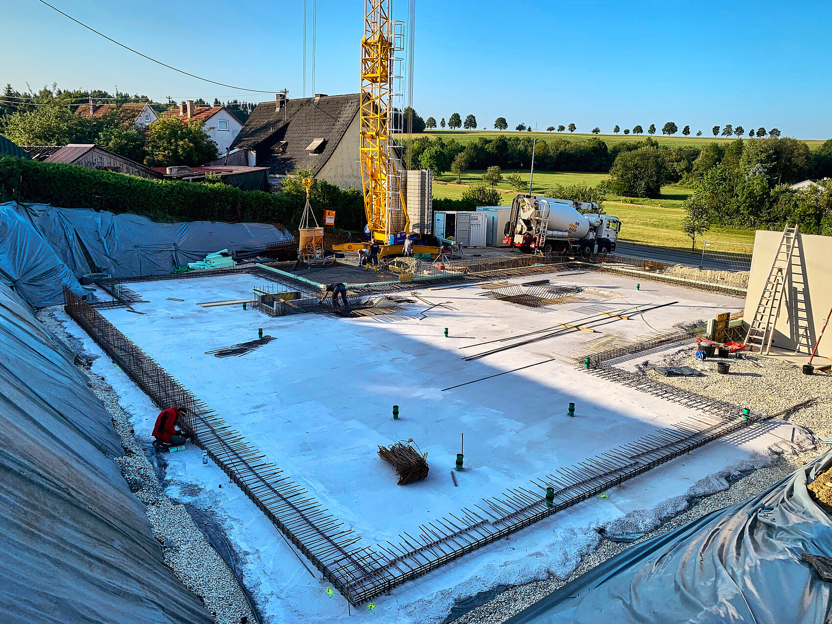 Construction site: concrete foundation with reinforcement, yellow crane, concrete mixer, workers.