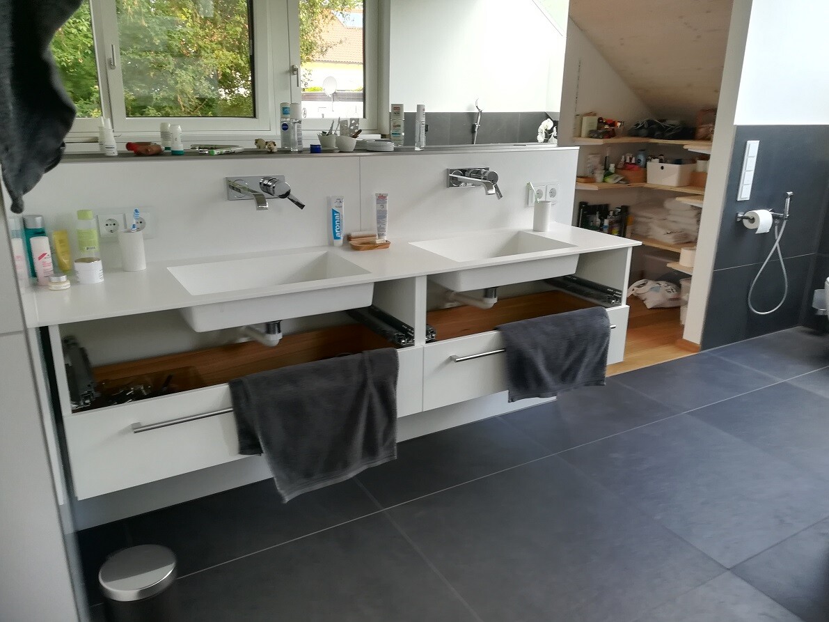 Modern double sink with open drawers, grey towels, shelf with personal care products.