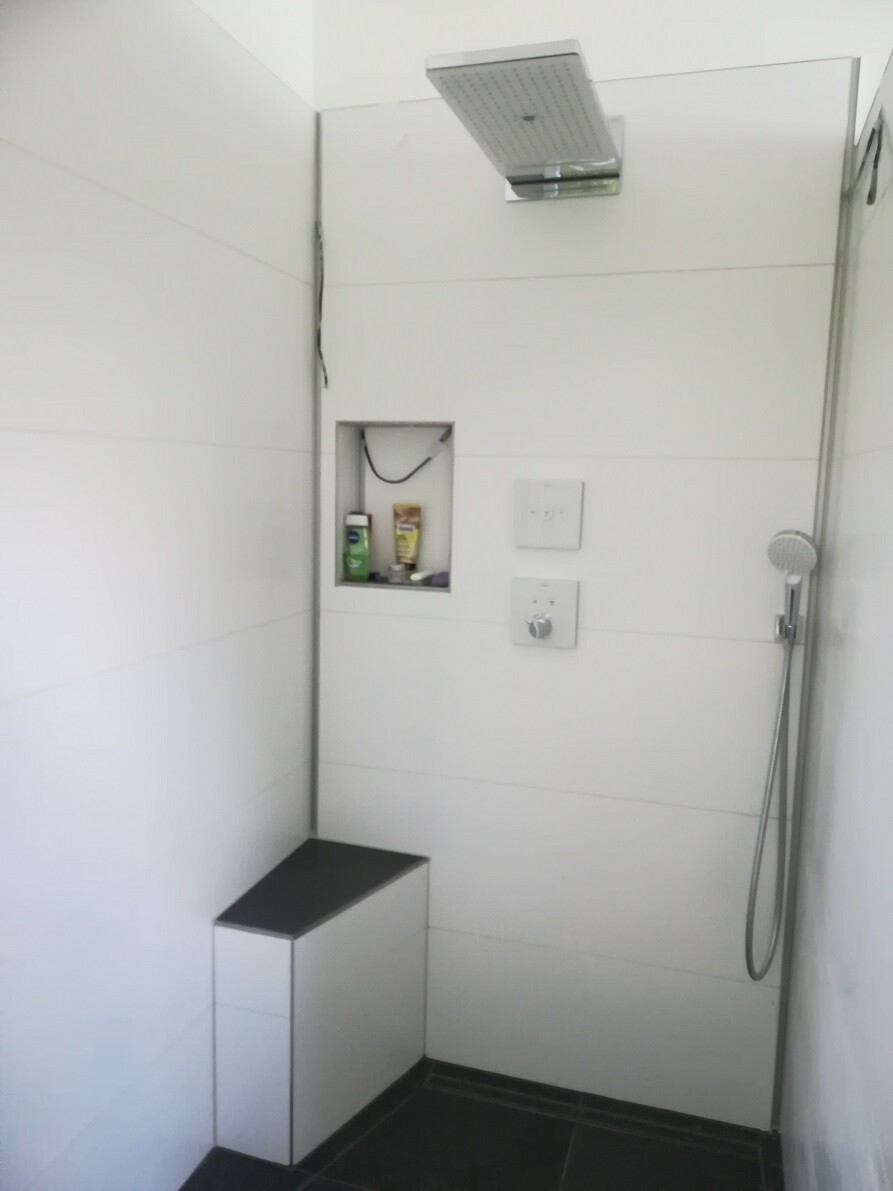 Walk-in shower with ceiling rain shower, handheld shower, niche with products, bench.