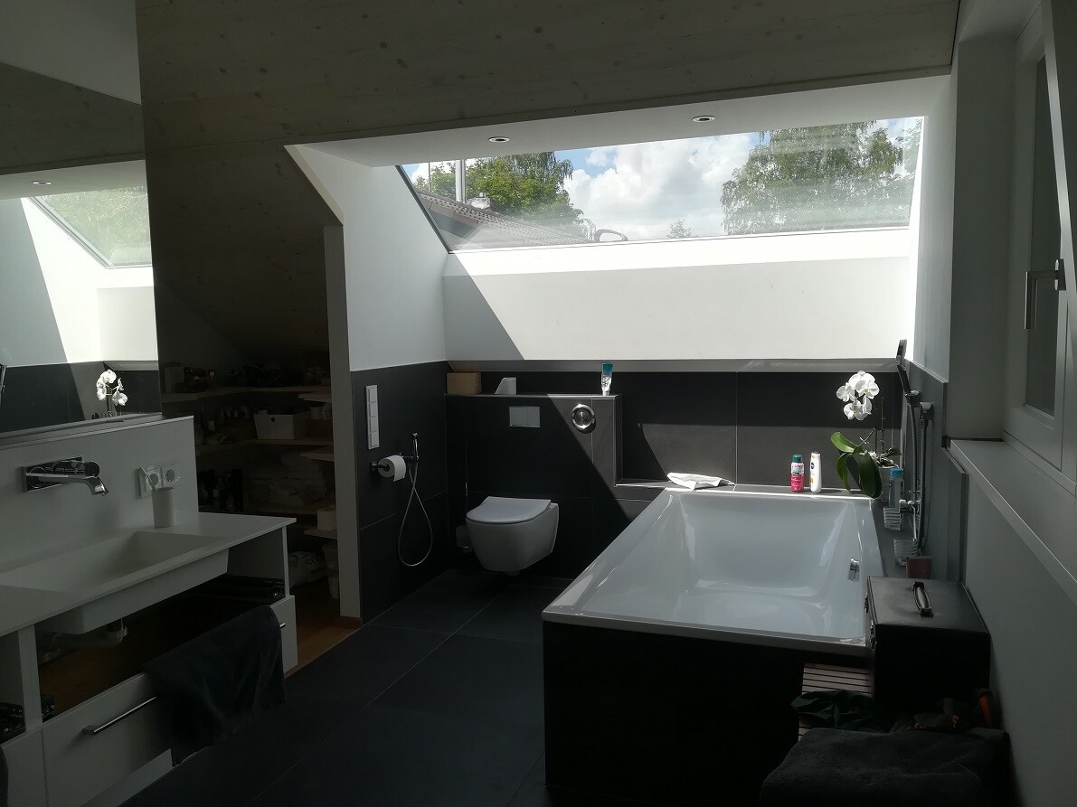 More modern bathroom with large bathtub under skylight, sink on the left, toilet in the middle.