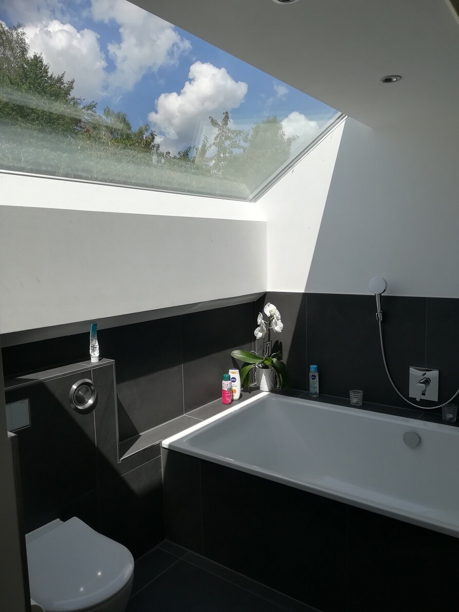 Modern bathroom with large skylight, bathtub, dark tiles and orchid.
