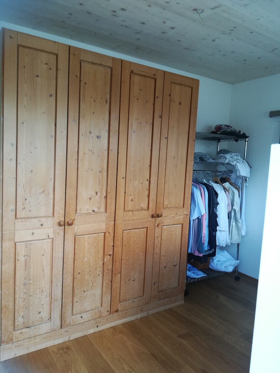 Large wooden wardrobe next to a clothes rail with hanging clothes in the bedroom