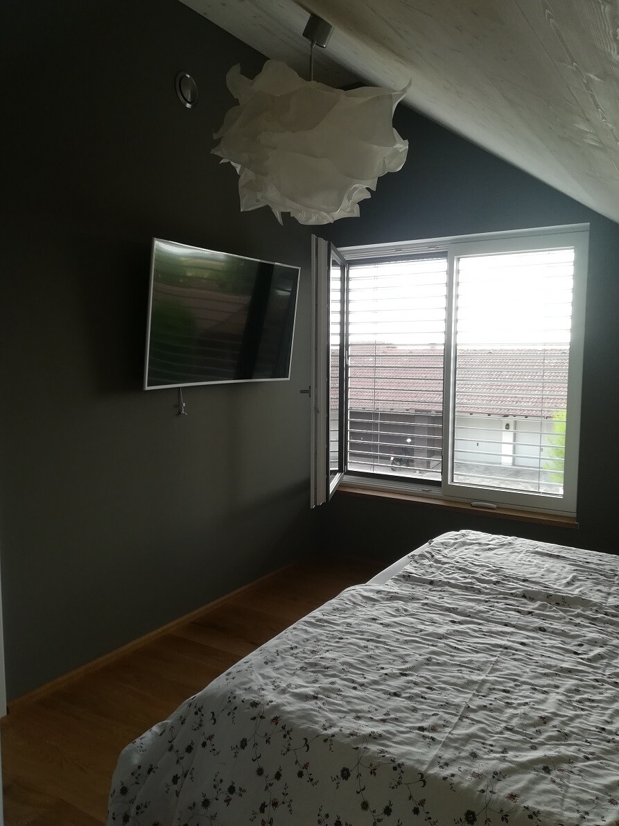 Bedroom with dark walls, wall-mounted TV, open window and bed with floral covering