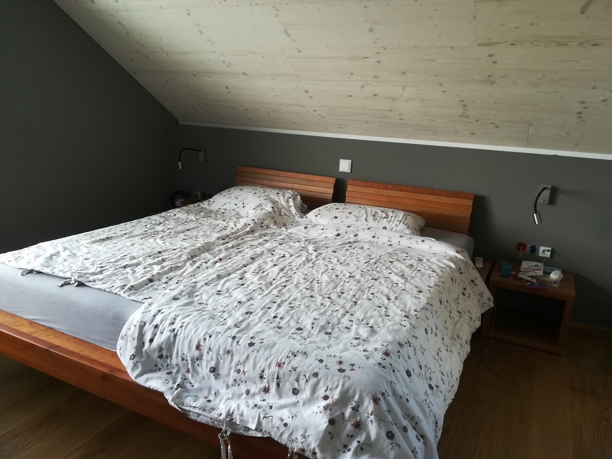 Double bed with white floral duvet, wooden frame, gray wall, bedside tables and lamps.