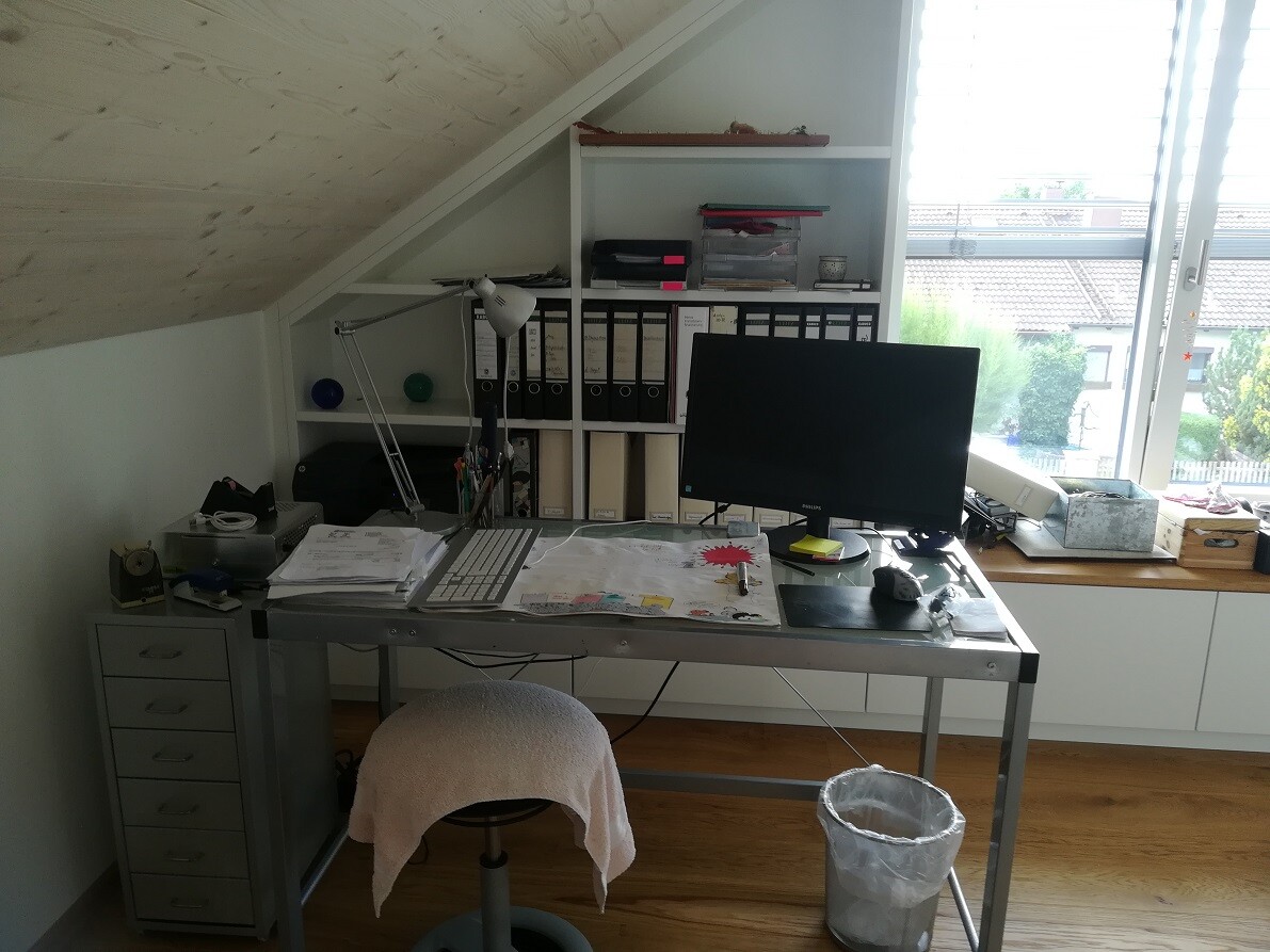 Desk in attic office with computer, folders, lamp and waste bin