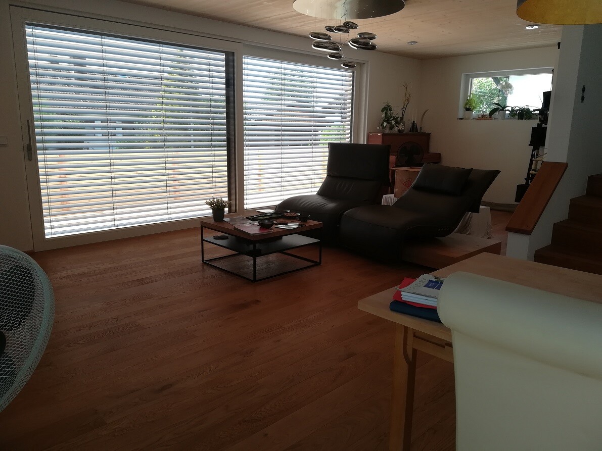 Living room with hardwood floor, large window front with blinds, two black recliners.