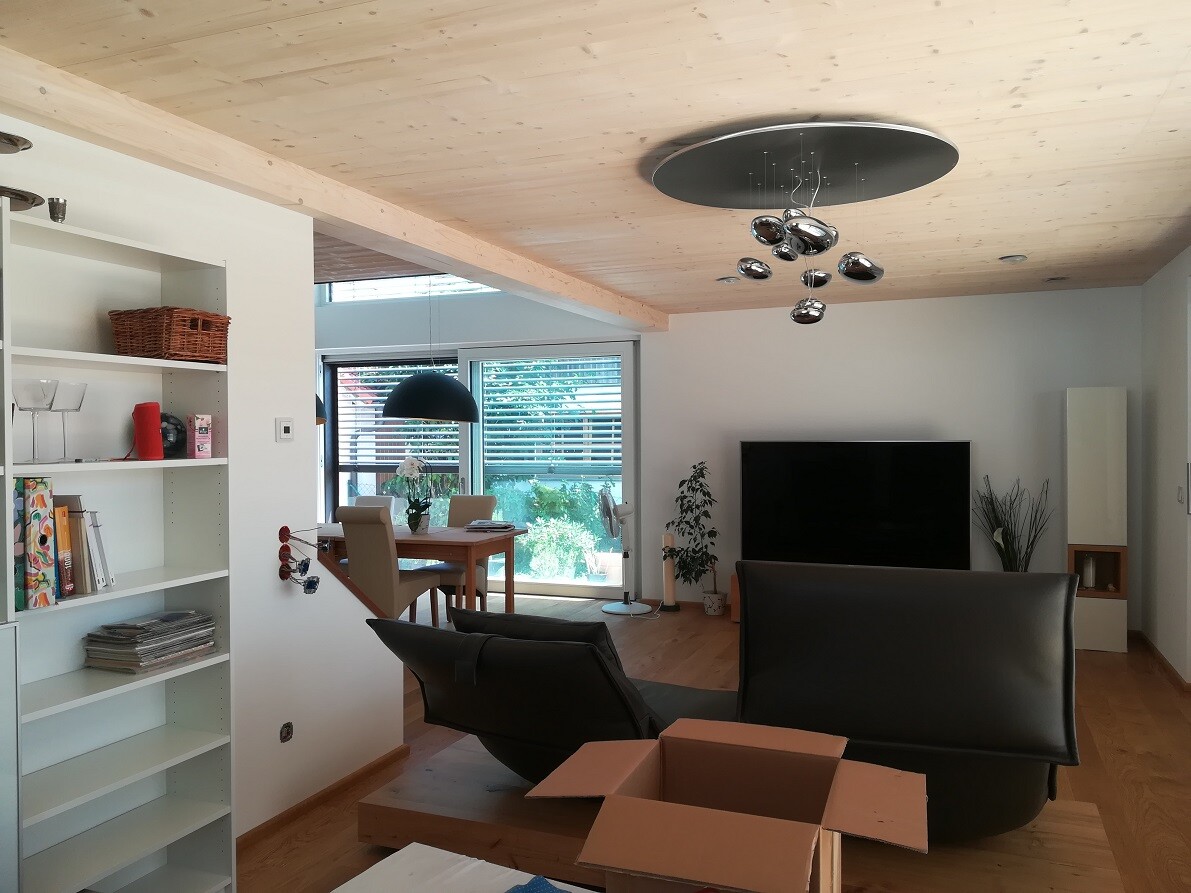 Bright living room with sofa, TV, dining table, bookshelf on the left, glass door to the garden, box.