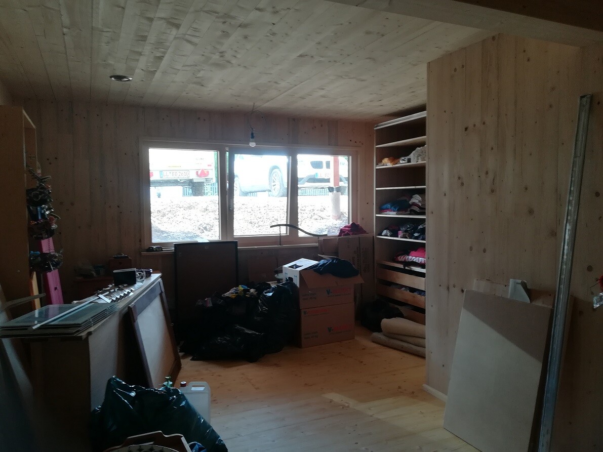 Wood storage room with shelves full of clothes, boxes, and garbage bags; window overlooking the construction site.