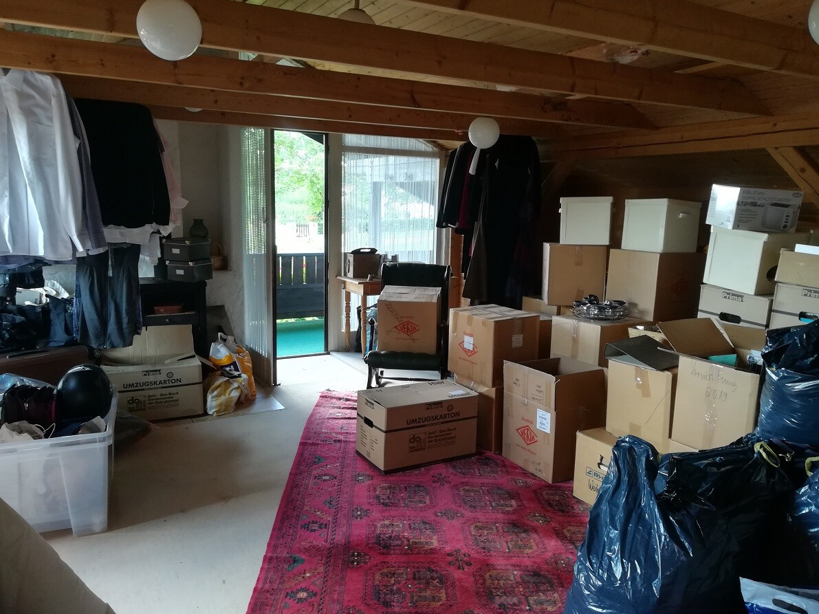 Attic storage room with boxes, clothes, and an open door to the garden.