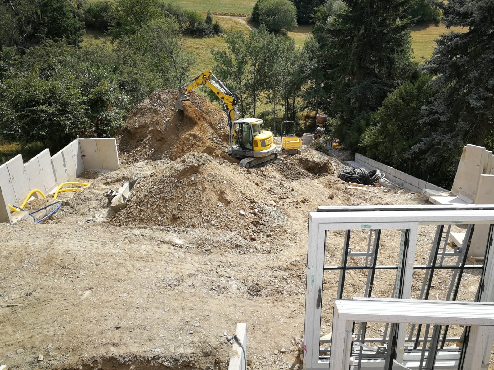 Small excavator shoveling soil on a construction site; concrete walls, framework and cable reels.