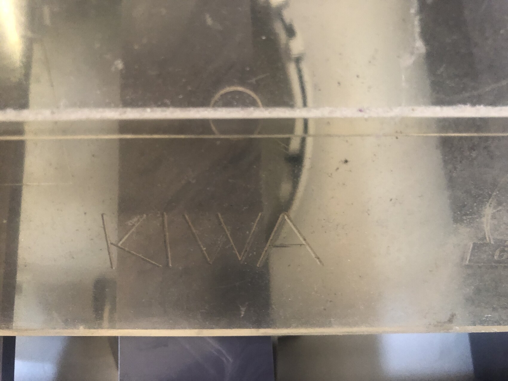 Close-up of a dusty metal surface with engraved letters in the lower left corner.