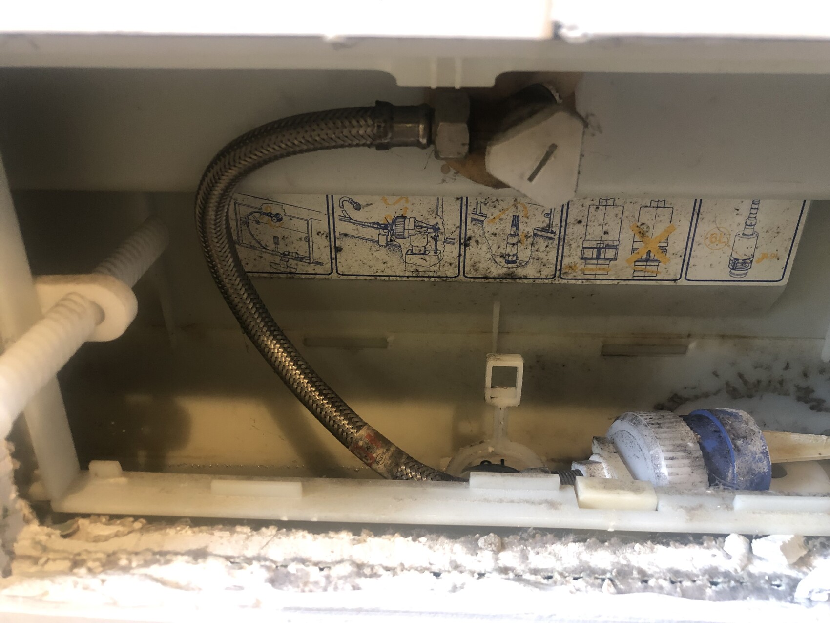 Interior of a device with stainless steel flexible hose, water connection, and diagram sticker.
