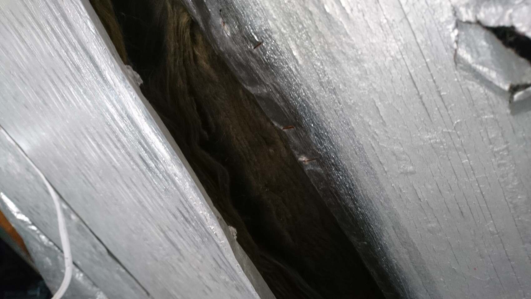 Close-up of grey painted wood with gap, dark cavity behind.