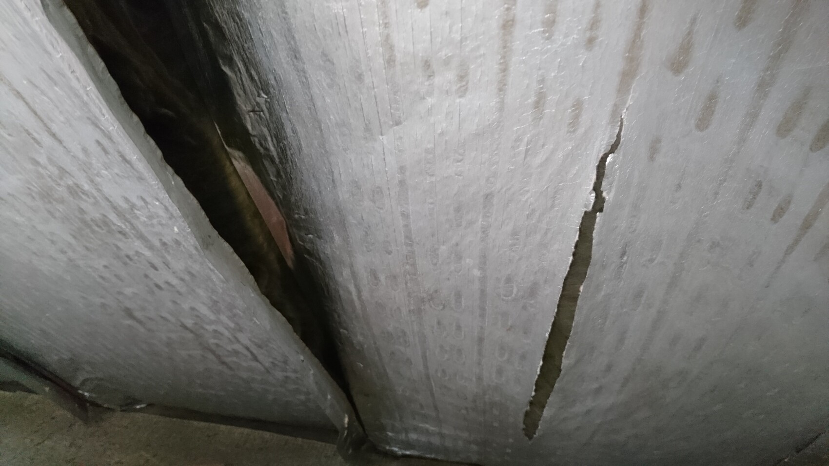 Large vertical crack in grey concrete wall with dark gap and rough surface
