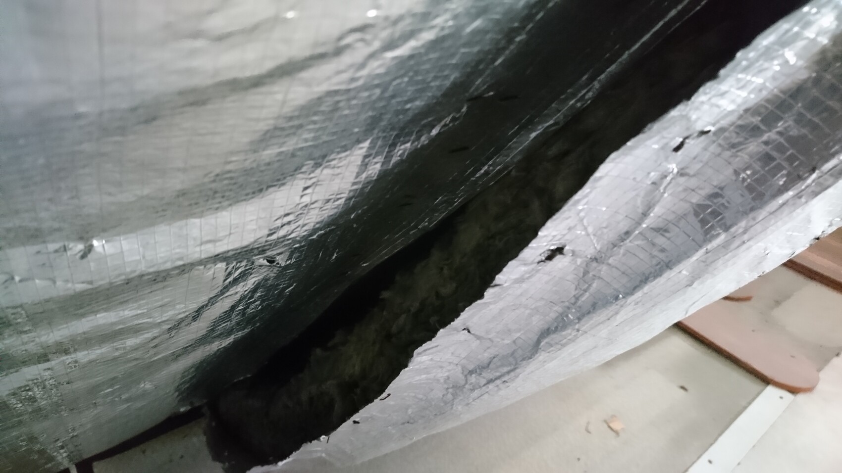 Close-up of silver insulating foil with cracks, dark gap underneath.