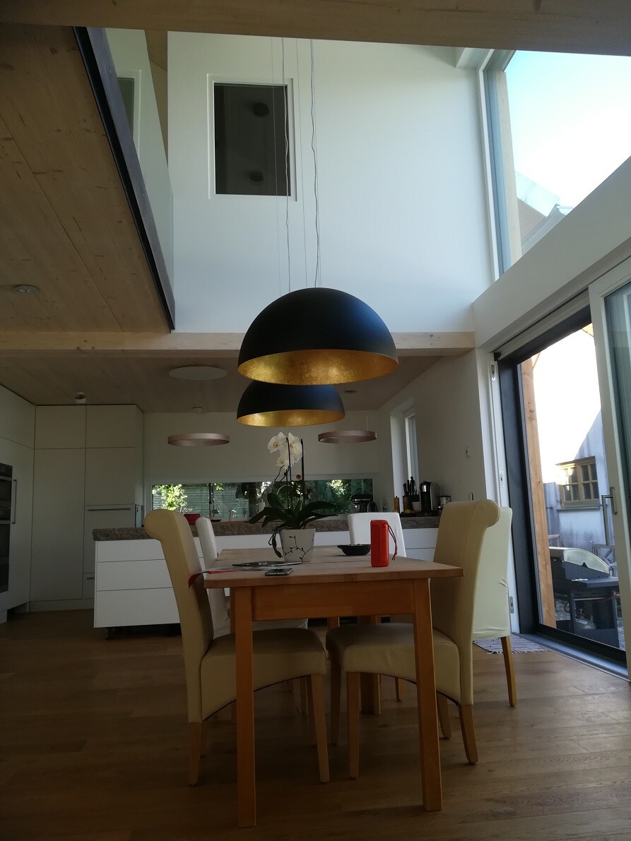 Open dining area: wooden table, cream-colored chairs, orchid, black lamps with gold inside.