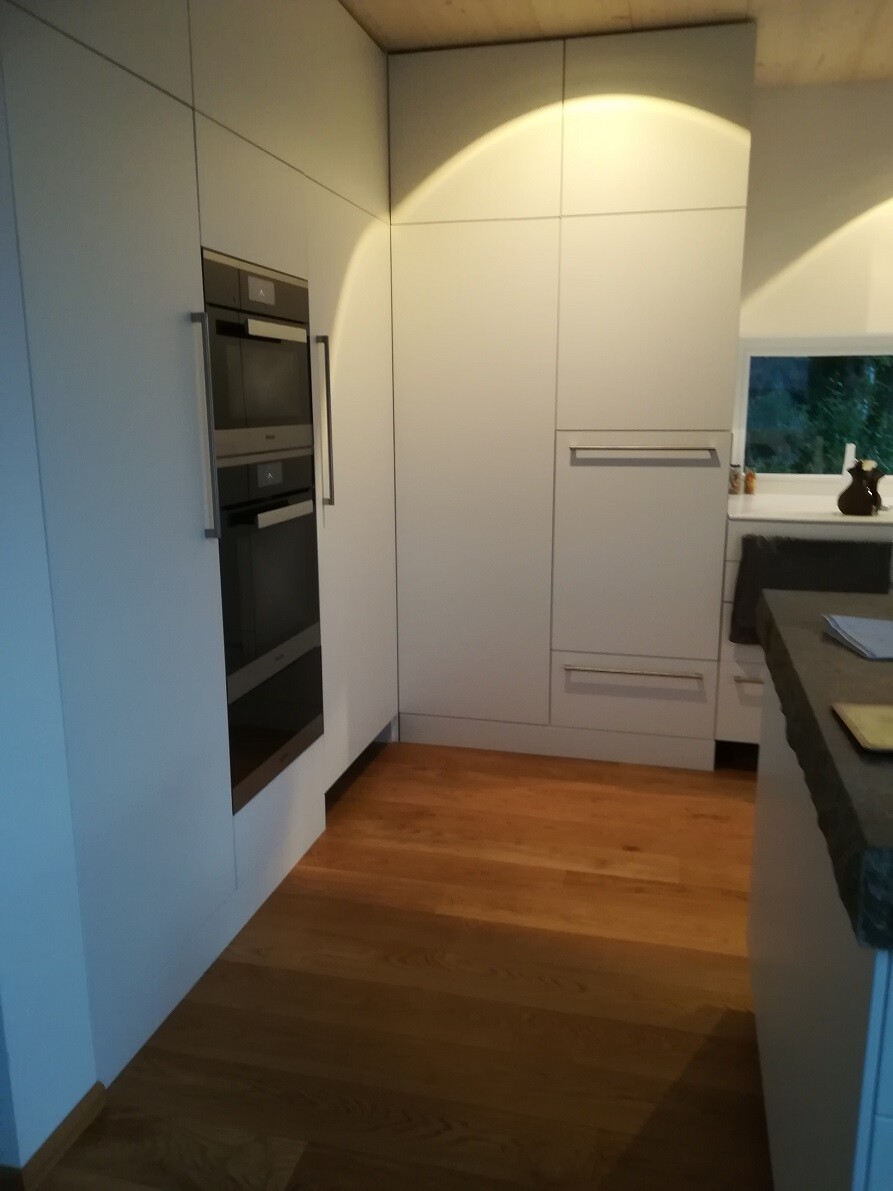 Modern kitchen: white cabinets, built-in ovens, wooden floor, kitchen island and window.
