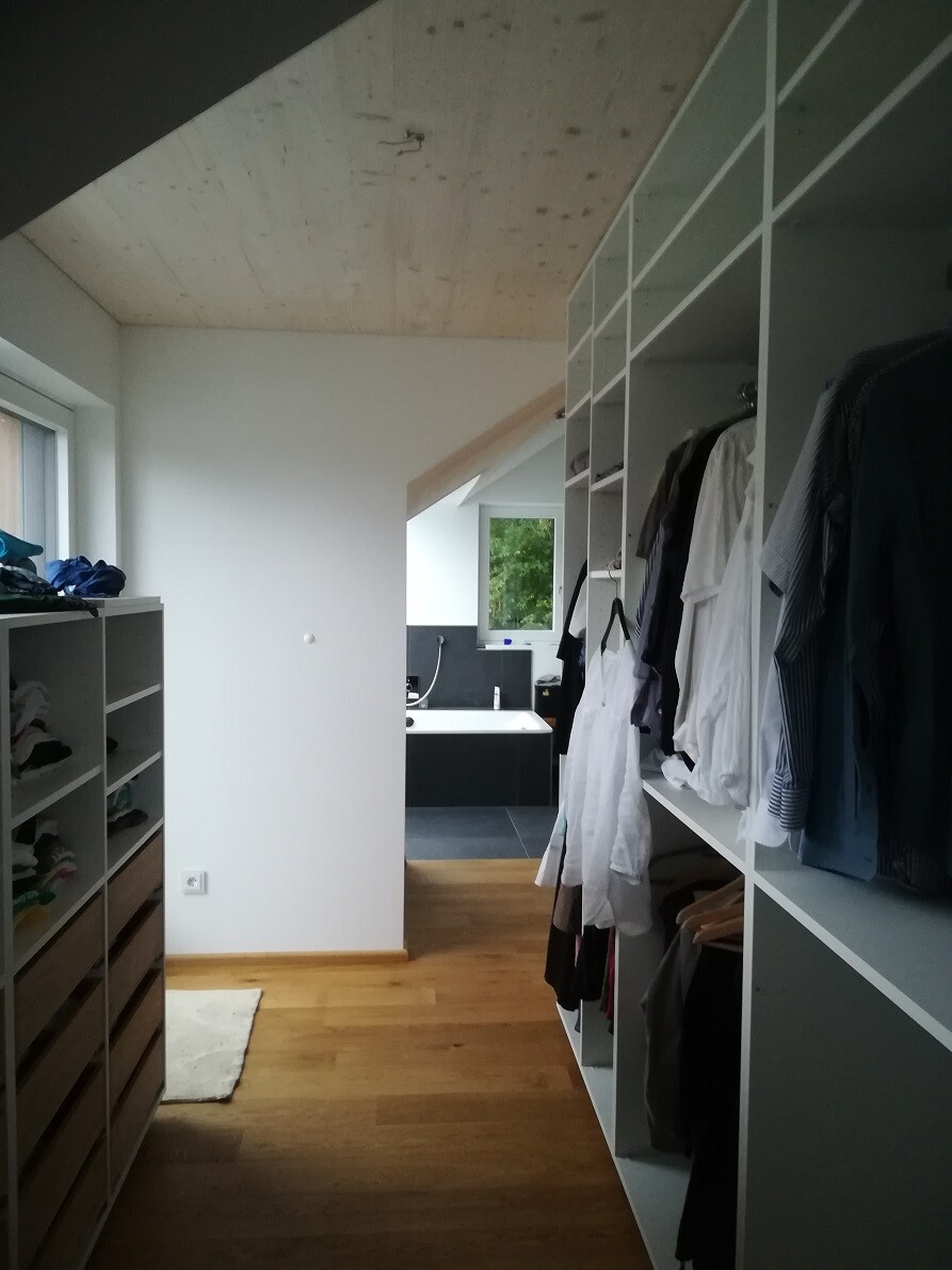 Wardrobe with open shelves full of clothes, wooden floor and view to bathroom at the end.