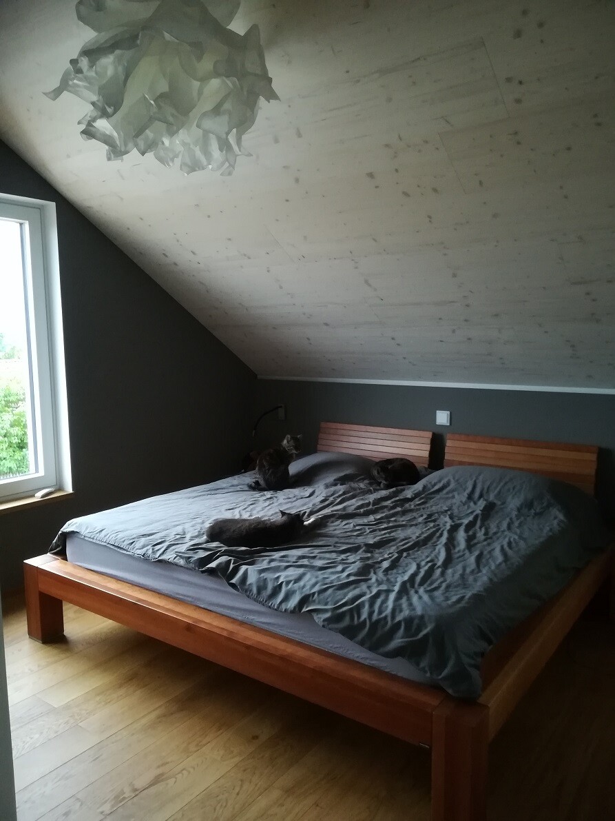 Bedroom with sloping ceiling, wooden bed with gray bedding, several cats sleeping on it.