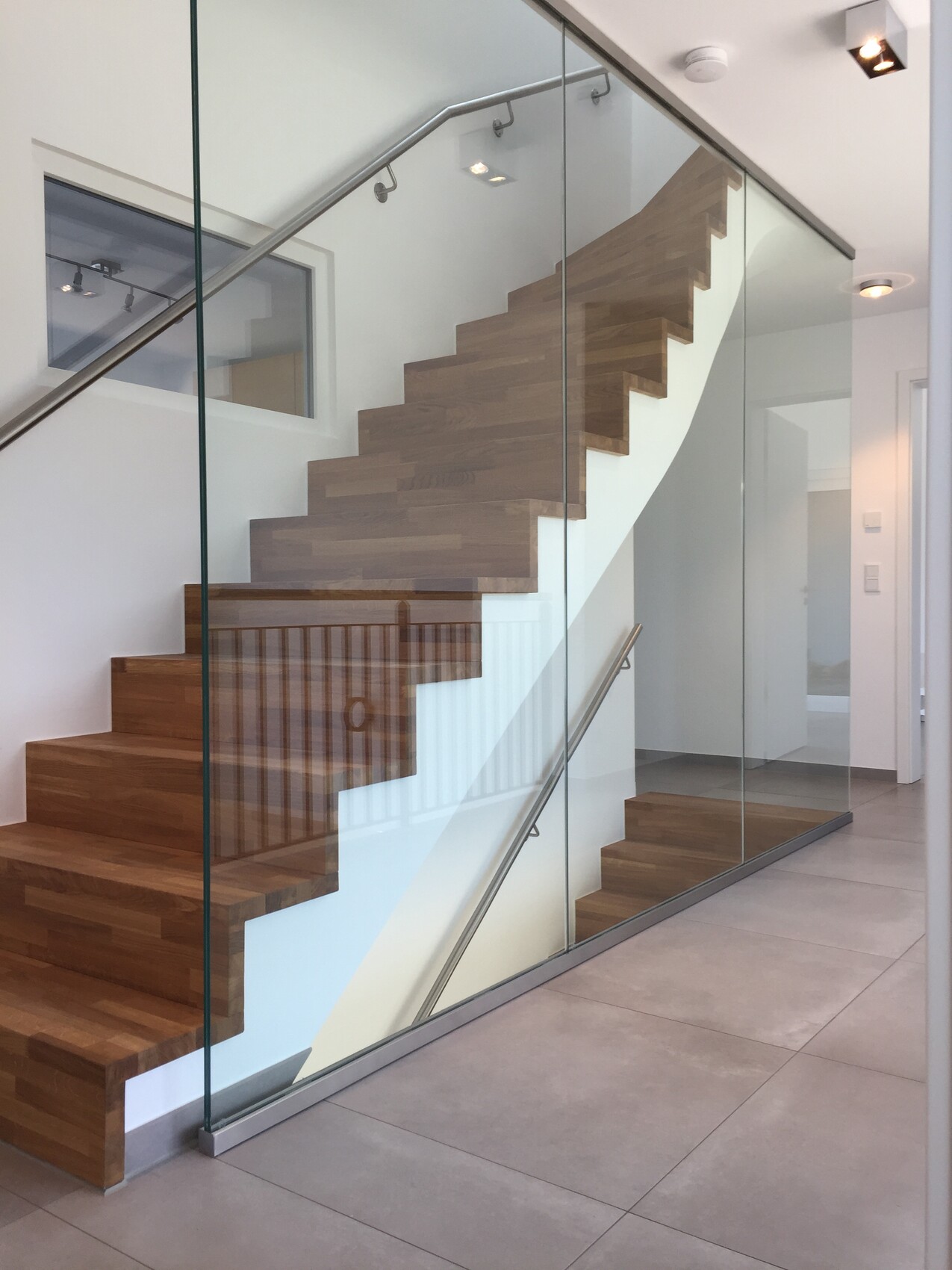 Modern wooden staircase with glass railing and metal handrail in a bright interior