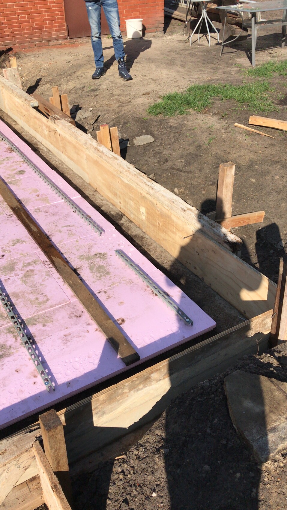 Baustelle mit Holzformwand, pinken Dämmplatten, Metallprofilen, nahe einer stehenden Person.