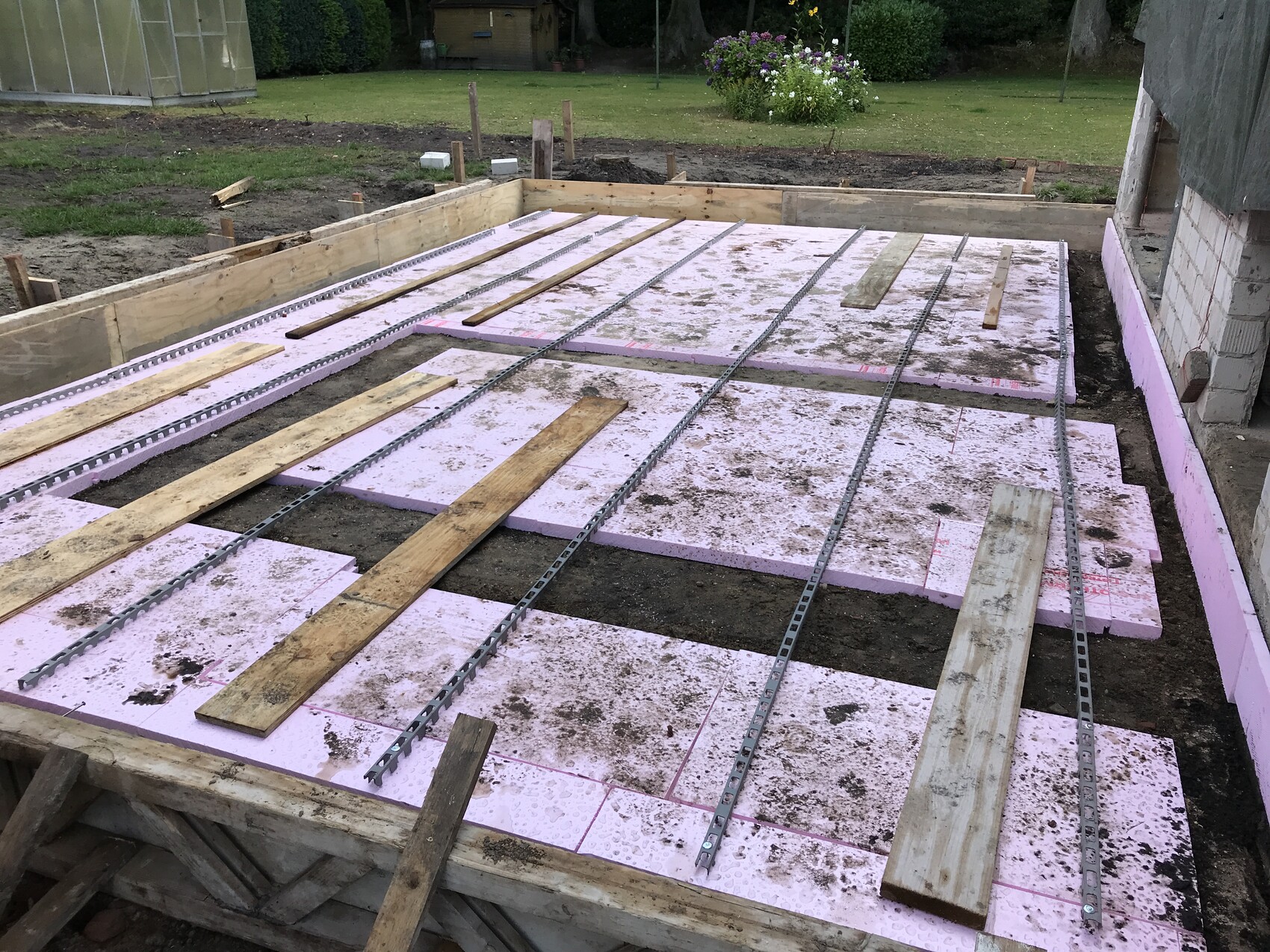 Fundamentplatte mit pinken Dämmplatten, Metallstreifen und Holzlatten auf einer Baugrube