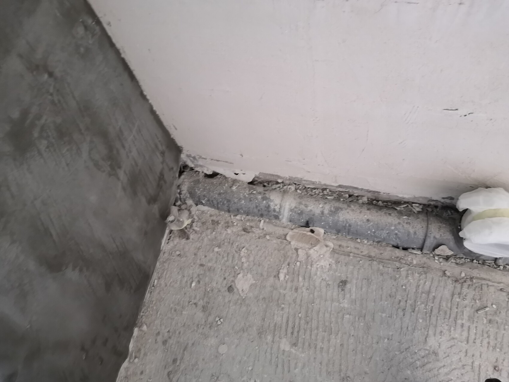 Bau-Ecke: schwarzes Rohr verlegt am Boden neben einer weißen Wand, Staub und Putzreste überall.