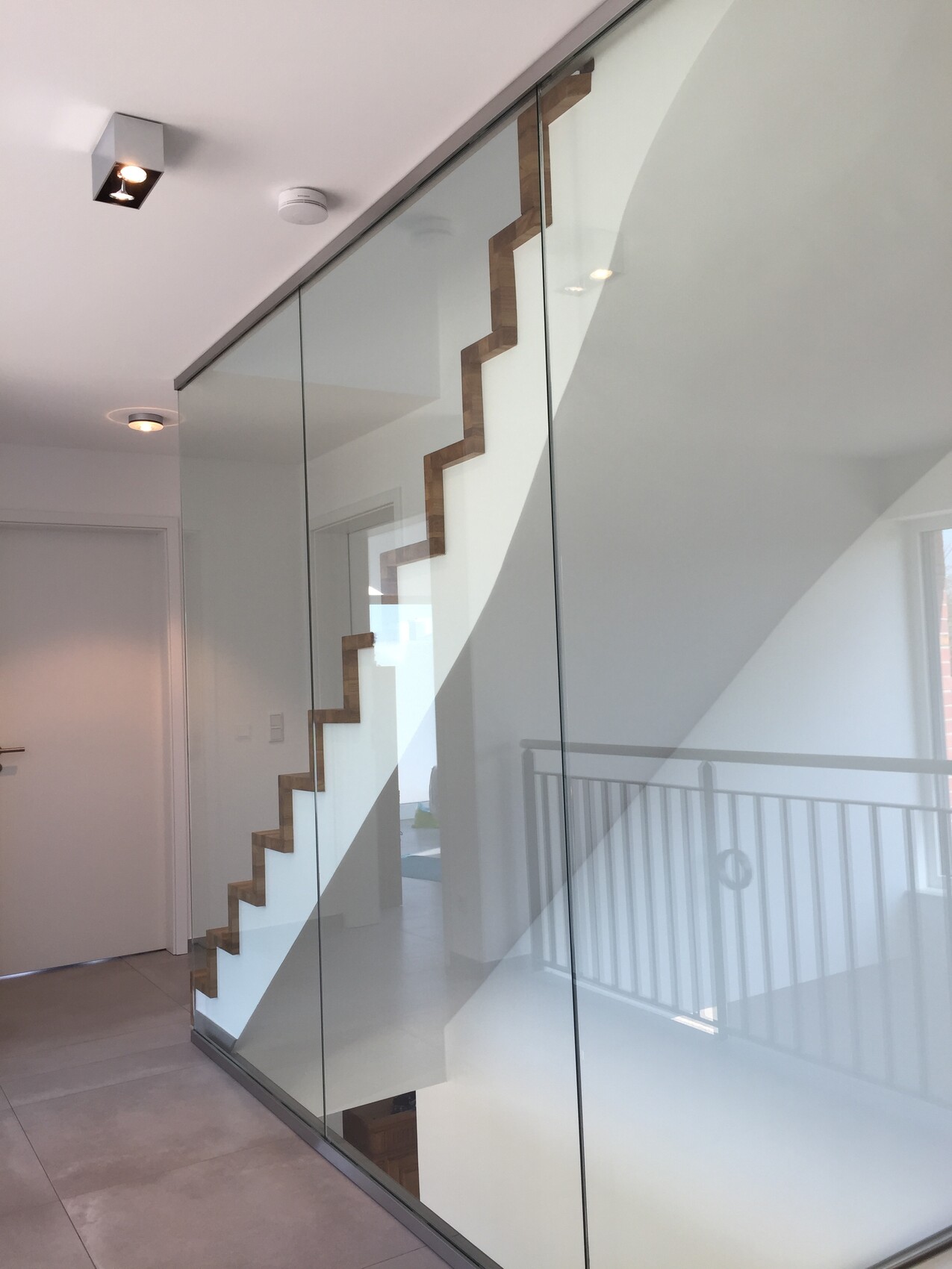 Modern interior view: glass wall with wooden zigzag staircase behind in bright apartment