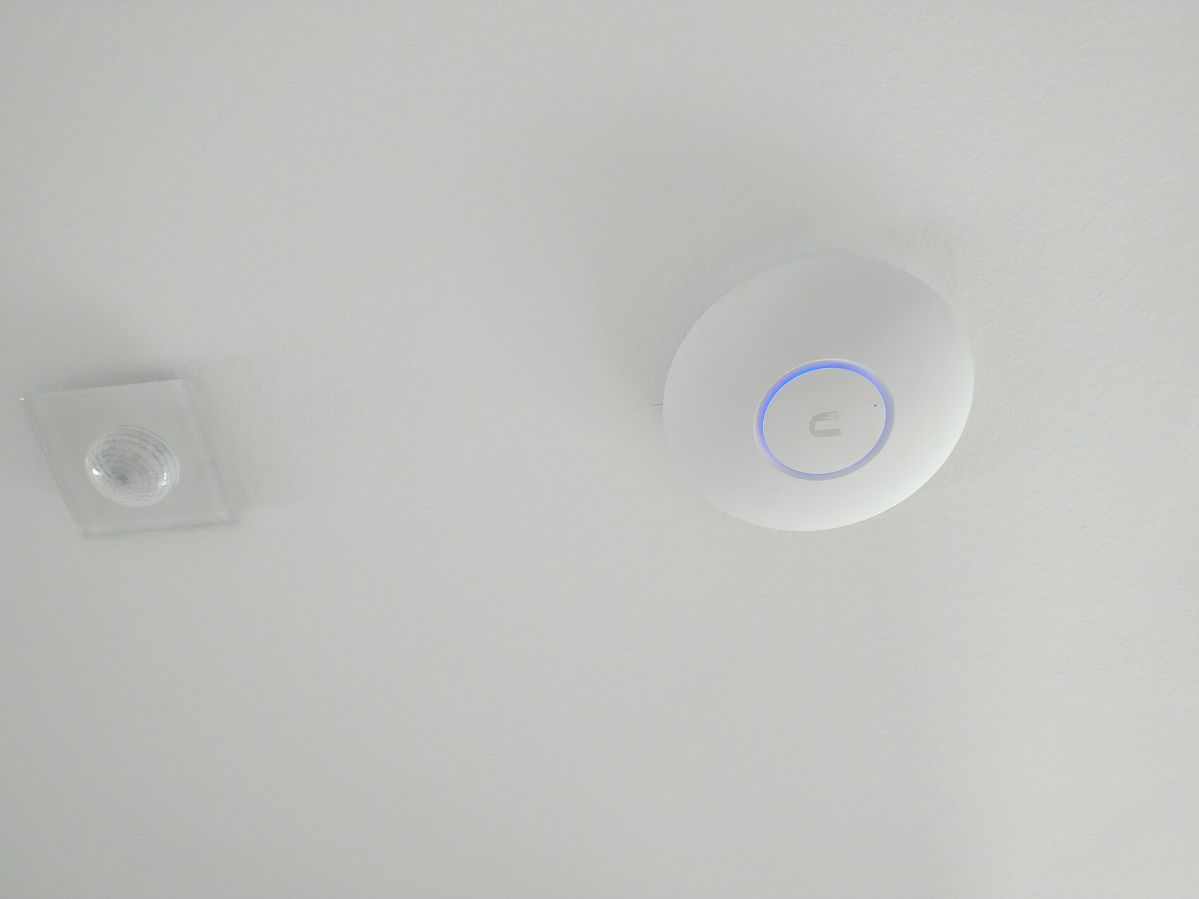 White ceiling with round safety sensor and blue light ring; recessed ceiling light on the left.