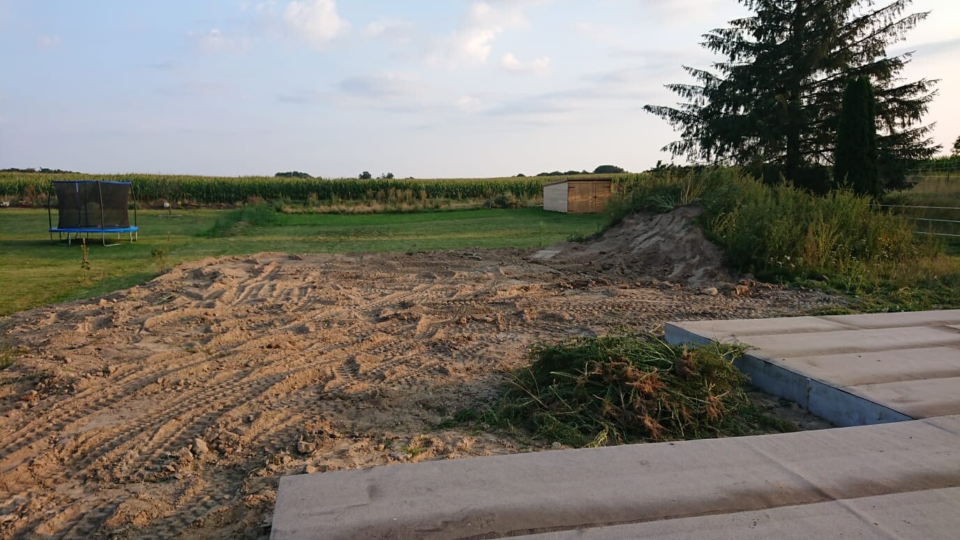 Open construction area with earthworks, concrete slabs and garden in the background.