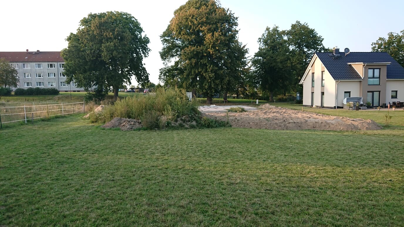 Green property with excavation pit and modern house in the background